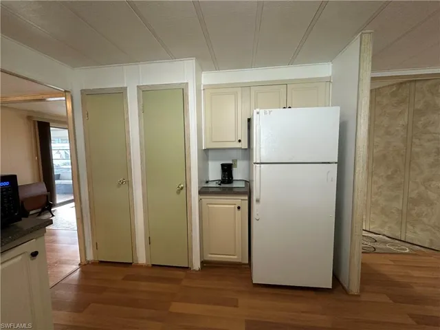 Kitchen with freestanding refrigerator, dark wood-type flooring, cream cabinetry, black microwave, and a textured ceiling