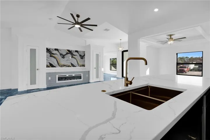 Kitchen featuring ceiling fan, light stone counters, a glass covered fireplace, a chandelier, and open floor plan