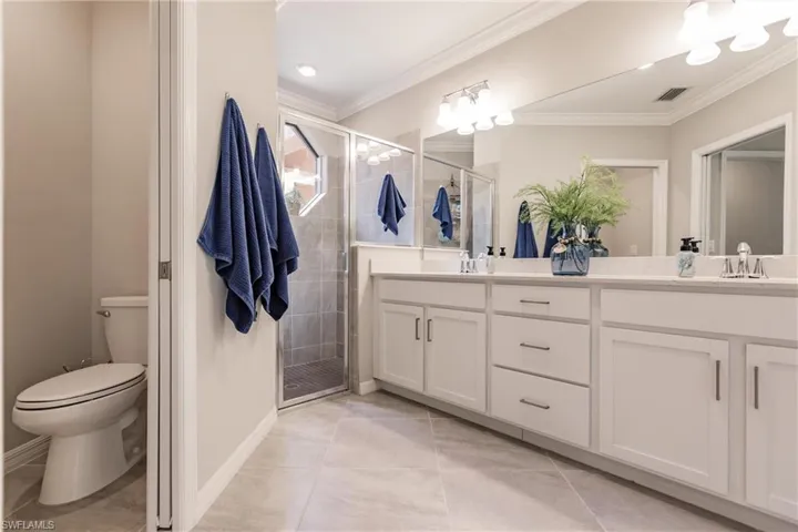 Master Bathroom with walk in shower, crown molding, toilet, dual sink  vanity, and tile patterned floors