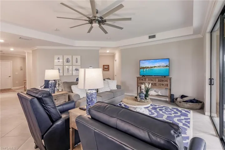 Living room with light tile patterned flooring, ceiling fan, crown molding, and a tray ceiling