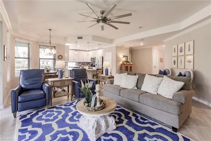 Tiled living room with ceiling fan with notable chandelier and ornamental molding