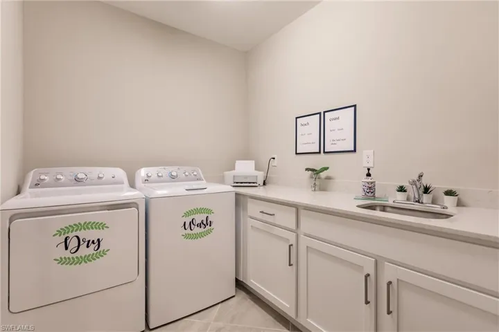 Clothes washing area with cabinets, light tile patterned floors, washer and clothes dryer, and sink