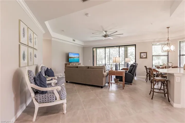 Living room featuring ceiling fan with notable chandelier, light tile patterned floors, a raised ceiling, and crown molding
