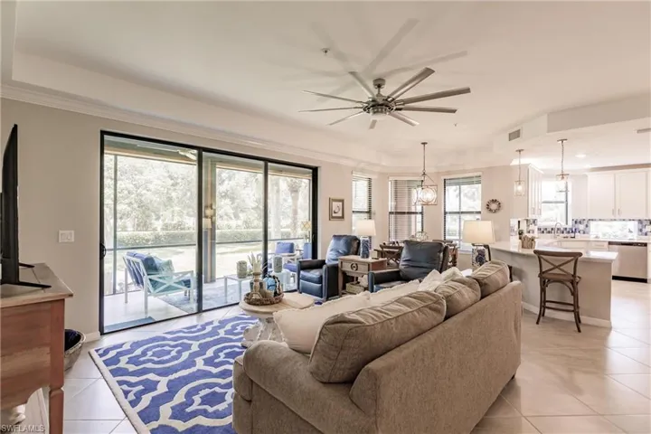 Tiled living room with ceiling fan with notable chandelier and crown molding