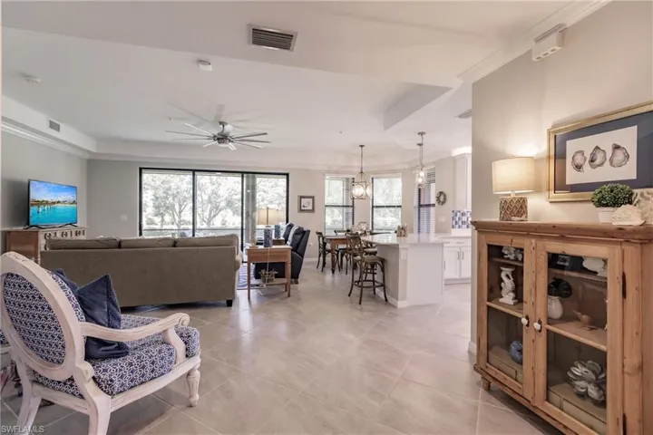 Tiled living room featuring a tray ceiling, crown molding, and ceiling fan with notable chandelier