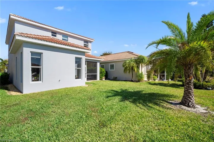 Back of house with stucco siding, a lawn, a tile roof, and a sunroom