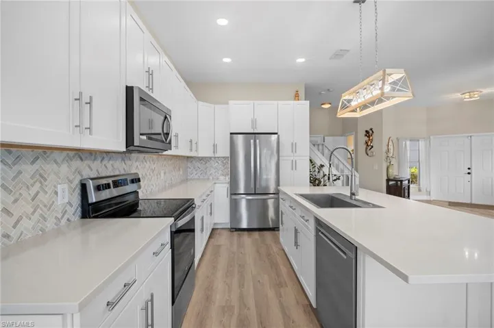Kitchen with stainless steel appliances, a kitchen island with sink, white cabinetry, decorative light fixtures, and light wood-style flooring