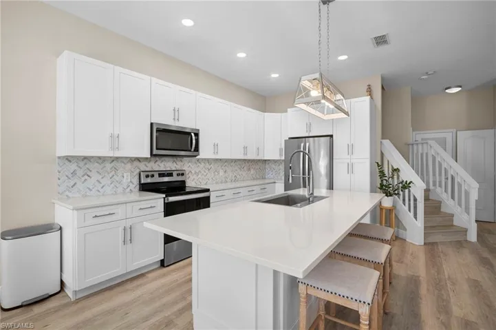 Kitchen with white cabinets, stainless steel appliances, a kitchen island with sink, and light wood finished floors