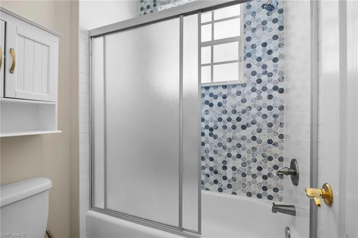 Bathroom with bath / shower combo with glass door and toilet