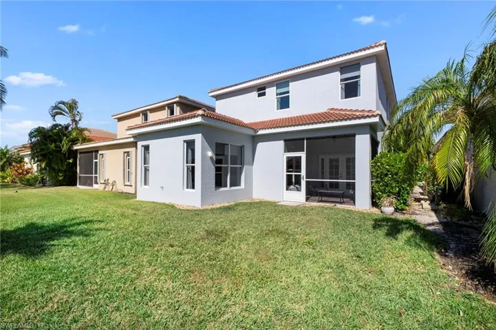 Rear view of property featuring a sunroom, stucco siding, a lawn, and a tile roof