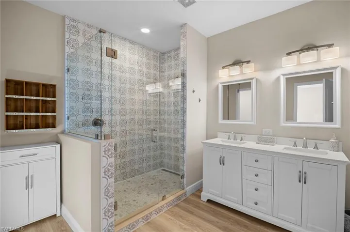 Bathroom featuring double vanity, a shower stall, and light wood-style flooring