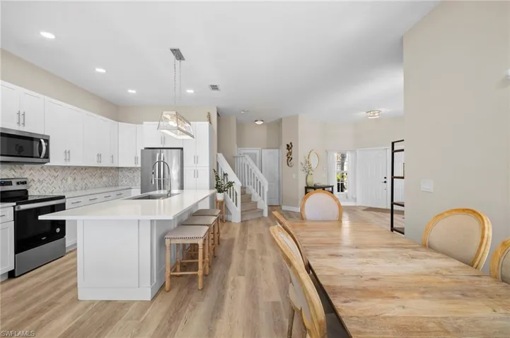 Kitchen featuring a breakfast bar, stainless steel appliances, white cabinetry, an island with sink, and light wood-style floors
