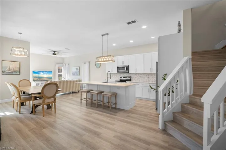 Kitchen with a center island with sink, hanging light fixtures, a breakfast bar, white cabinets, and stainless steel appliances