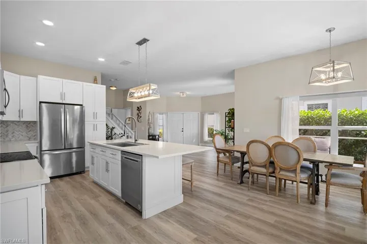 Kitchen featuring a center island with sink, suspended lighting, stainless steel appliances, and white cabinetry