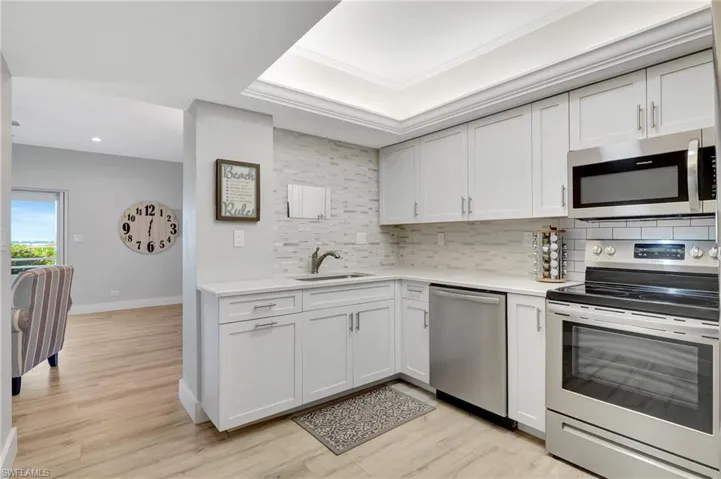 Kitchen with white cabinetry, tasteful backsplash, stainless steel appliances, light wood-type flooring, and sink