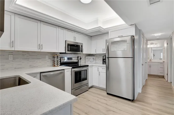 Kitchen with white cabinetry, tasteful backsplash, ornamental molding, appliances with stainless steel finishes, and light hardwood / wood-style flooring