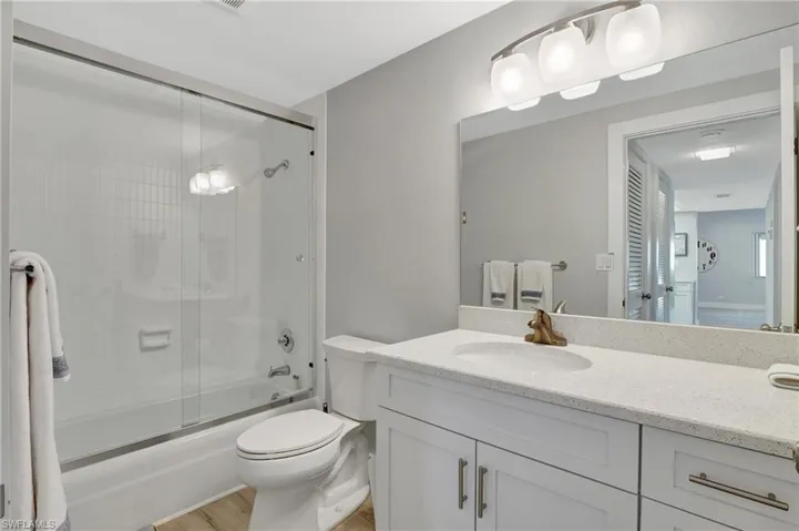Full bathroom with toilet, hardwood / wood-style floors, vanity, and combined bath / shower with glass door