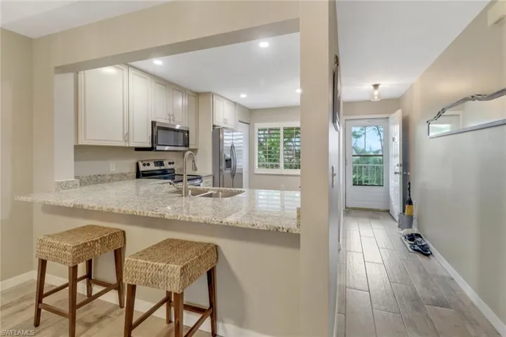 Kitchen featuring light stone counters, white cabinets, stainless steel appliances, light wood-type flooring, and a kitchen bar