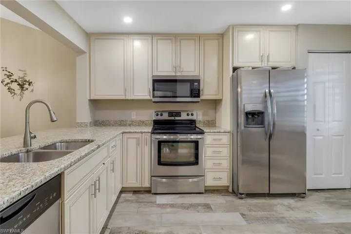 Kitchen featuring light stone countertops, cream cabinets, appliances with stainless steel finishes, and sink