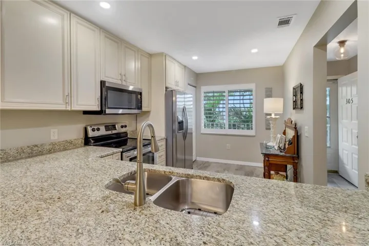 Kitchen with light wood-type flooring, light stone counters, appliances with stainless steel finishes, and sink
