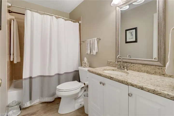 Full bathroom with hardwood / wood-style floors, shower / tub combo with curtain, vanity, and toilet
