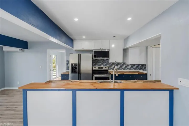 Kitchen featuring appliances with stainless steel finishes, tasteful backsplash, white cabinetry, sink, and wooden counters