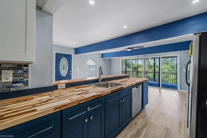 Kitchen with butcher block countertops, sink, appliances with stainless steel finishes, white cabinetry, and tasteful backsplash