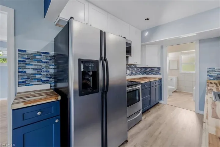 Kitchen with stainless steel appliances, white cabinetry, blue cabinets, and wooden counters