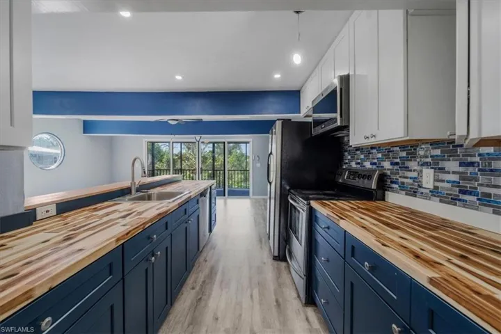 Kitchen with stainless steel appliances, sink, white cabinets, and wooden counters