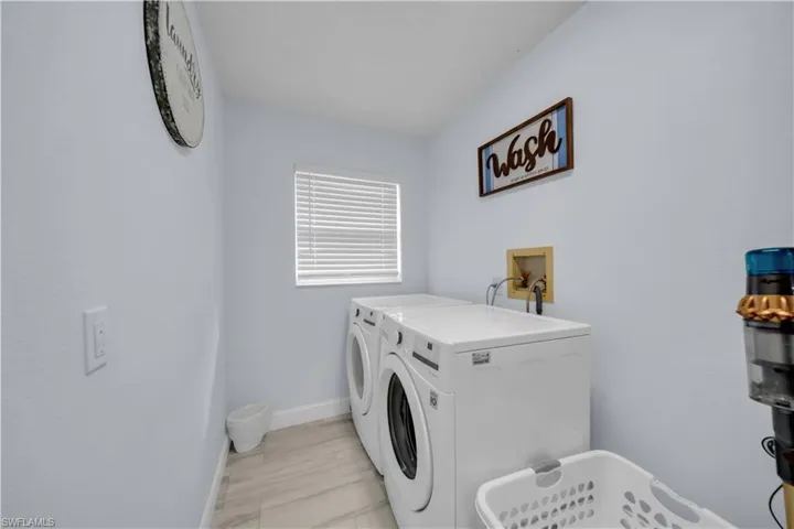 Dedicated laundry area featuring a window with blinds, light blue wall paint, and wood-finish tile flooring