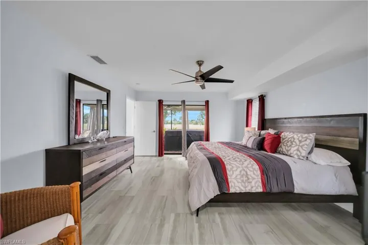 Spacious bedroom featuring light wood-finish flooring, a ceiling fan, and sliding glass doors leading to an exterior area