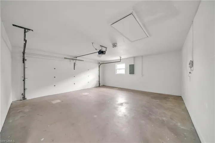 Spacious garage with an overhead door, automatic opener, concrete flooring, and a ceiling-mounted access panel
