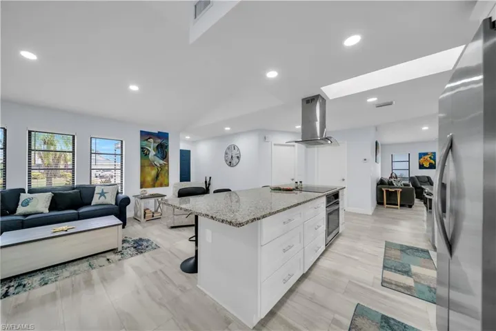 Modern kitchen island featuring a granite-style countertop, white cabinetry with chrome hardware, and a stainless steel range hood