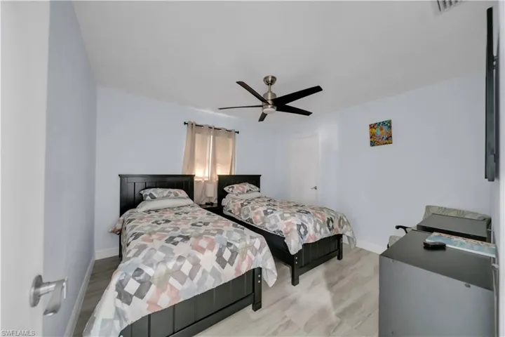 Bedroom featuring light blue walls, wood-finish flooring, and a ceiling fan with integrated lighting