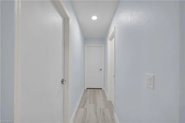 Hallway with light-toned walls, recessed lighting, and wood-finish flooring