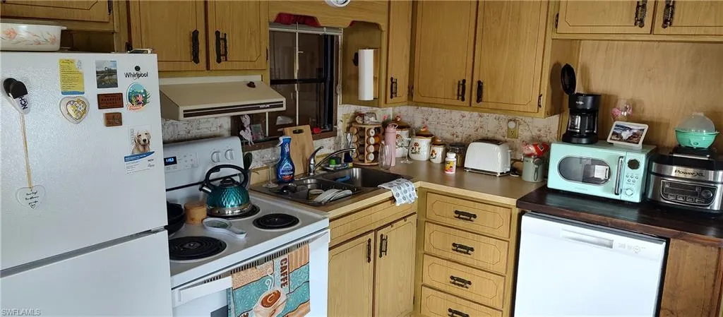Kitchen with white appliances, range hood, and light countertops