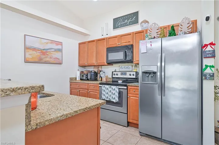 Kitchen with stainless steel appliances, light stone countertops, light tile patterned floors, and brown cabinets