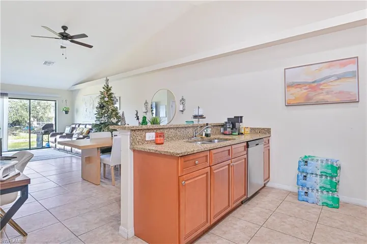 Kitchen with a peninsula, brown cabinetry, lofted ceiling, light stone counters, and ceiling fan