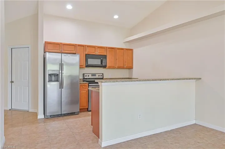Kitchen featuring stainless steel appliances, brown cabinetry, light tile patterned floors, light stone countertops, and high vaulted ceiling