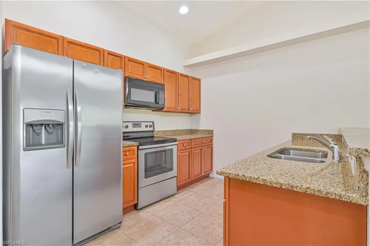 Unit #613 Kitchen with stainless steel appliances, light stone counters, light tile patterned floors, brown cabinets, and recessed lighting