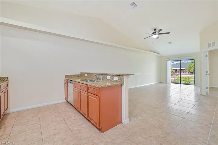 Kitchen featuring a peninsula, vaulted ceiling, light stone countertops, light tile patterned floors, and brown cabinetry