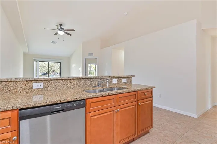 Kitchen with dishwasher, light stone counters, brown cabinets, vaulted ceiling, and a ceiling fan