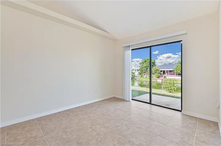 Empty room with a water view, vaulted ceiling, and light tile patterned floors