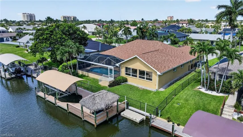 Waterfront property featuring a screened-in pool, multiple covered boat lifts, and a thatched-roof tiki hut