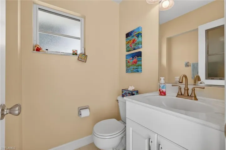 Powder room featuring a white single-sink vanity with a gold-tone faucet, a mirror, and a window with privacy glass