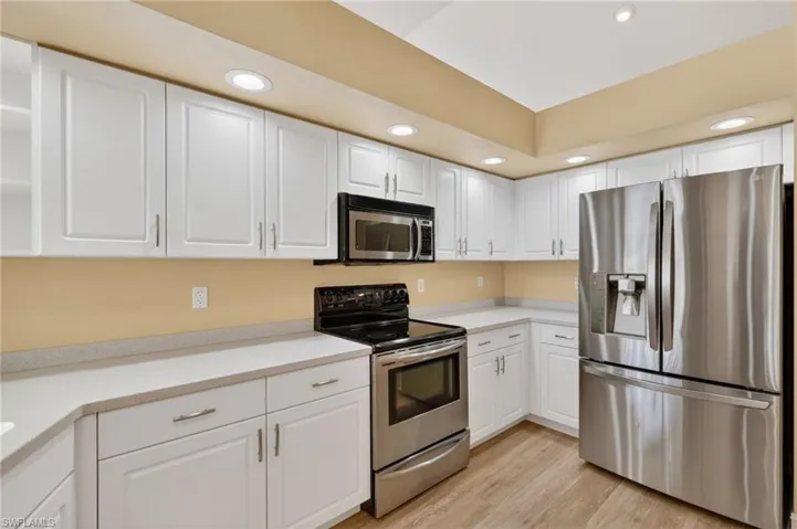 Bright kitchen featuring white cabinetry with silver hardware, light-toned countertops, and wood-finish flooring