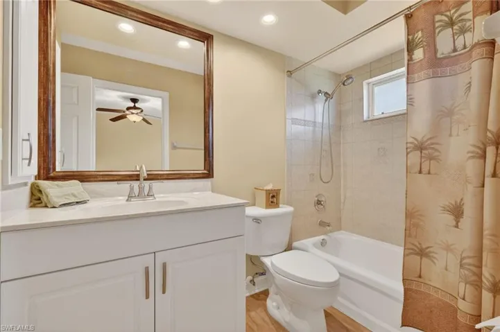 Bathroom featuring a white vanity with a light-toned countertop, a framed wall mirror, a toilet, a bathtub with a shower fixture, and a tiled shower surround