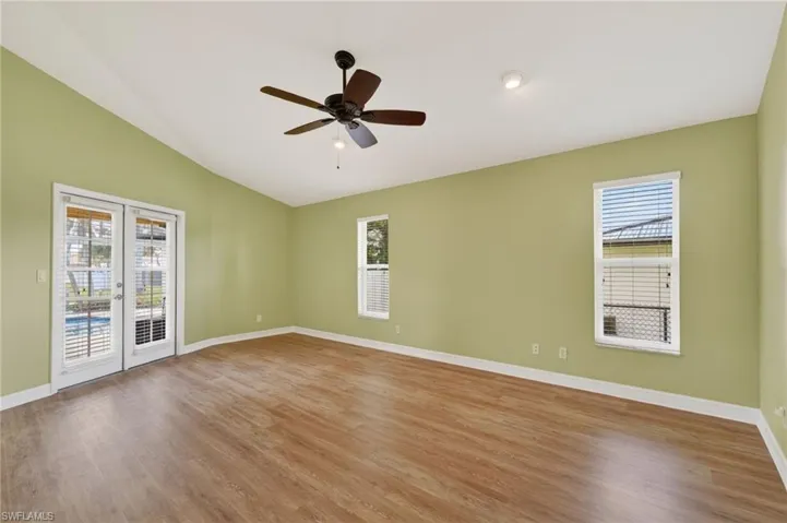 Spacious room featuring wood-finish flooring, light green walls, a vaulted ceiling, and dual French doors opening to a pool area