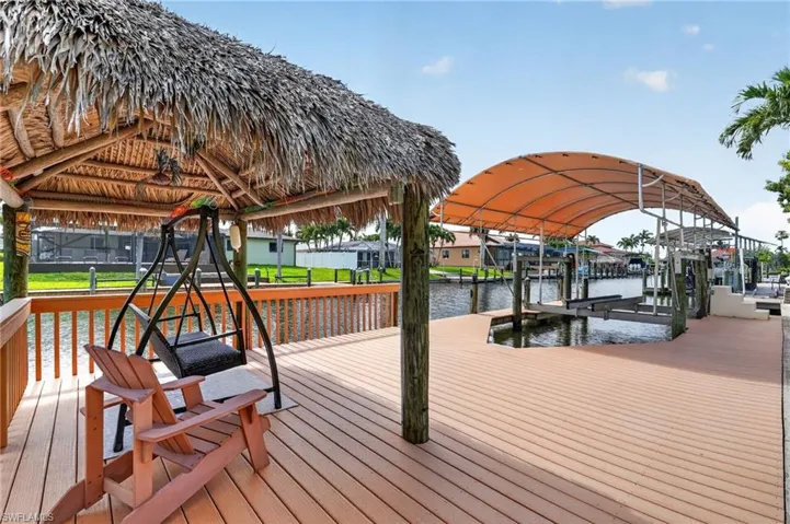 Expansive waterfront deck featuring a thatched-roof tiki hut, dedicated boat lift with canopy, composite wood decking, and a wood railing system