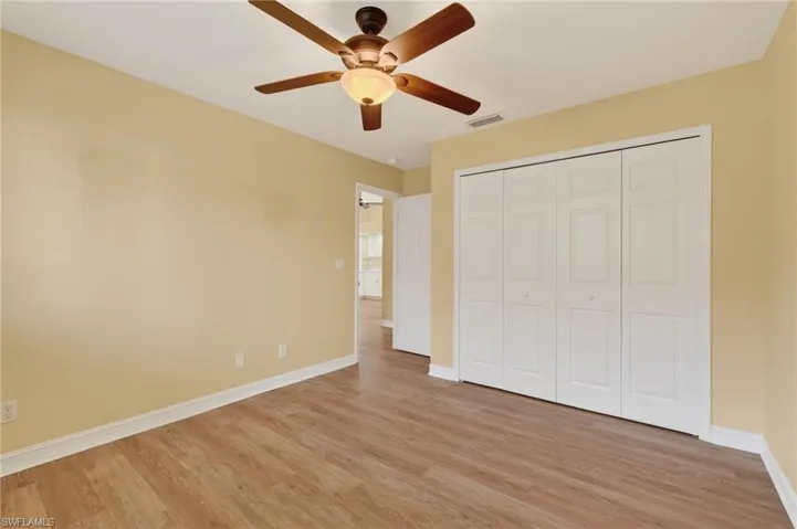 Spacious room featuring wood-finish flooring, light-colored walls, white baseboards, and a ceiling fan with integrated lighting